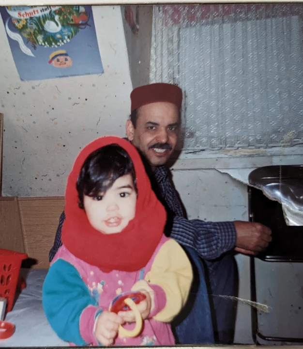 Dorcaf as a child holding a toy, with an adult behind her